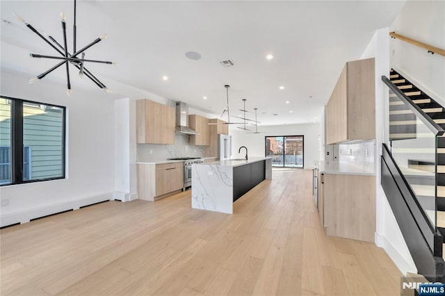 kitchen with high end stainless steel range, sink, hanging light fixtures, a kitchen island with sink, and wall chimney range hood