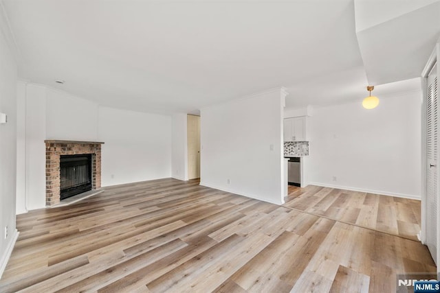 unfurnished living room featuring crown molding, a brick fireplace, and light wood-type flooring