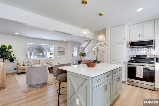 kitchen featuring light hardwood / wood-style flooring, appliances with stainless steel finishes, hanging light fixtures, backsplash, and a kitchen island