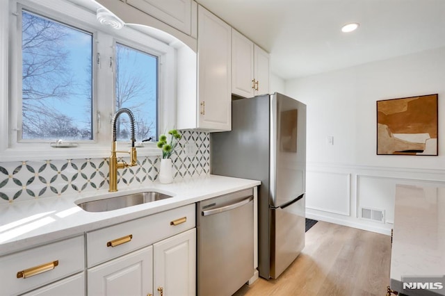 kitchen featuring sink, white cabinetry, light stone counters, stainless steel appliances, and light hardwood / wood-style floors