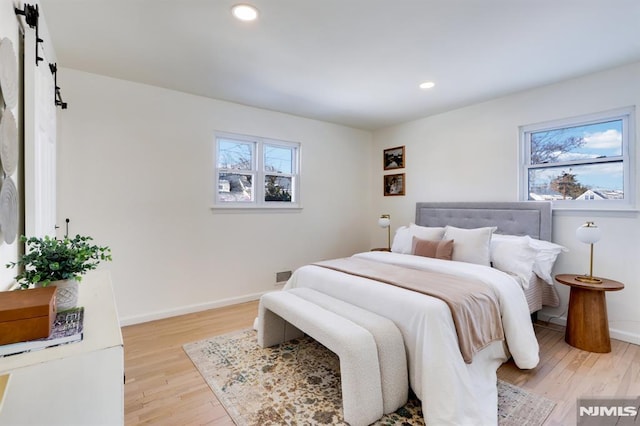 bedroom with a barn door, light hardwood / wood-style floors, and multiple windows