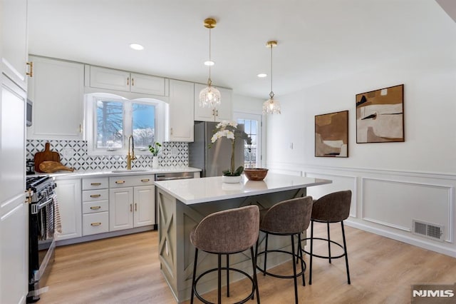 kitchen with a kitchen island, decorative light fixtures, white cabinetry, sink, and stainless steel appliances