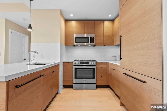 kitchen featuring appliances with stainless steel finishes, sink, decorative backsplash, hanging light fixtures, and light hardwood / wood-style flooring