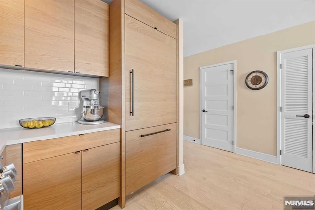 kitchen with light wood finished floors, baseboards, light brown cabinetry, light countertops, and decorative backsplash