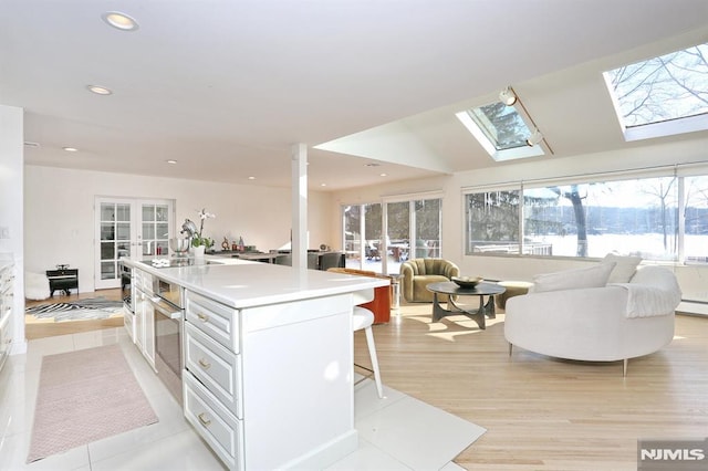 kitchen with vaulted ceiling with skylight, an island with sink, a breakfast bar area, white cabinets, and french doors