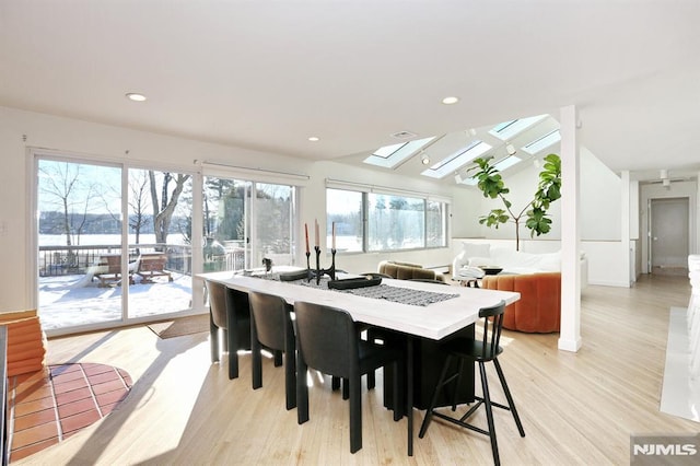 dining room with a water view, lofted ceiling with skylight, and light wood-type flooring