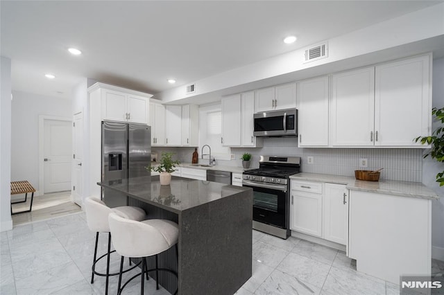 kitchen with white cabinetry, a kitchen island, dark stone counters, and appliances with stainless steel finishes