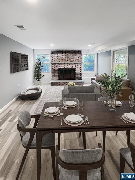 dining space with hardwood / wood-style floors, a wealth of natural light, and a brick fireplace