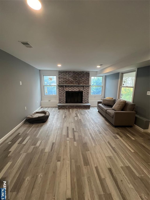 unfurnished living room with wood-type flooring and a brick fireplace