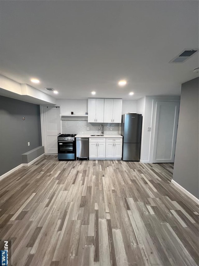 kitchen with sink, tasteful backsplash, light wood-type flooring, appliances with stainless steel finishes, and white cabinets