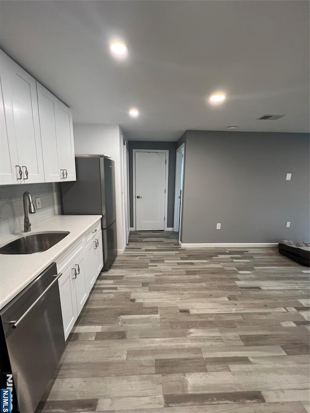 kitchen with stainless steel appliances, white cabinetry, sink, and light wood-type flooring