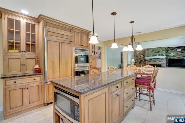 kitchen with pendant lighting, dark stone countertops, light tile patterned floors, glass insert cabinets, and built in appliances