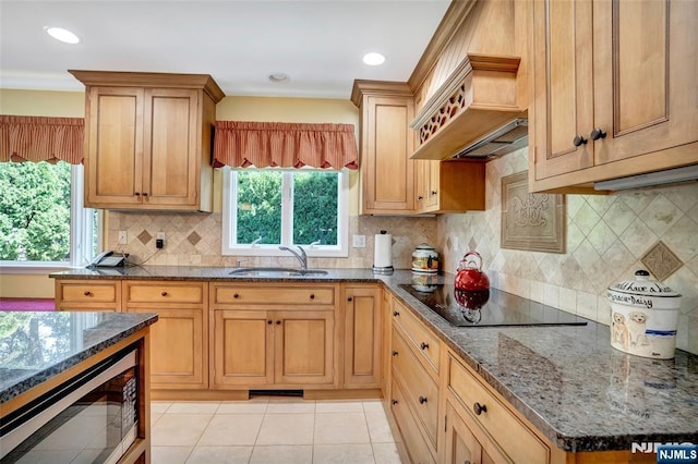 kitchen featuring premium range hood, a sink, stainless steel microwave, dark stone counters, and black electric cooktop