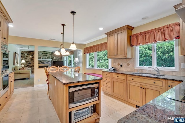 kitchen featuring a sink, stainless steel microwave, backsplash, open floor plan, and dark stone counters