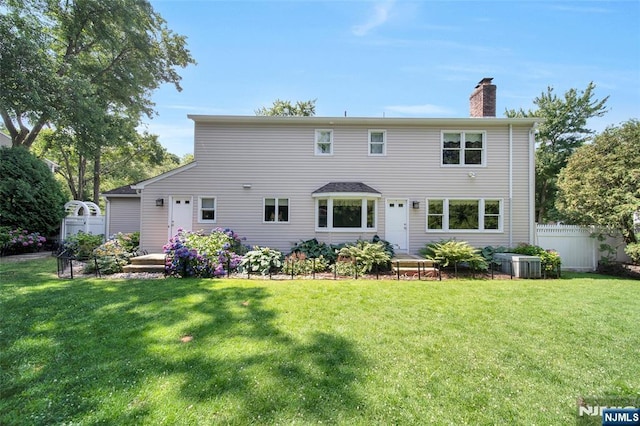 rear view of property featuring central AC unit, a yard, fence, and a chimney