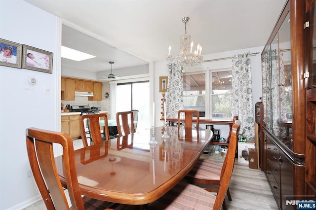 dining space featuring light hardwood / wood-style floors, a wealth of natural light, a chandelier, and a skylight