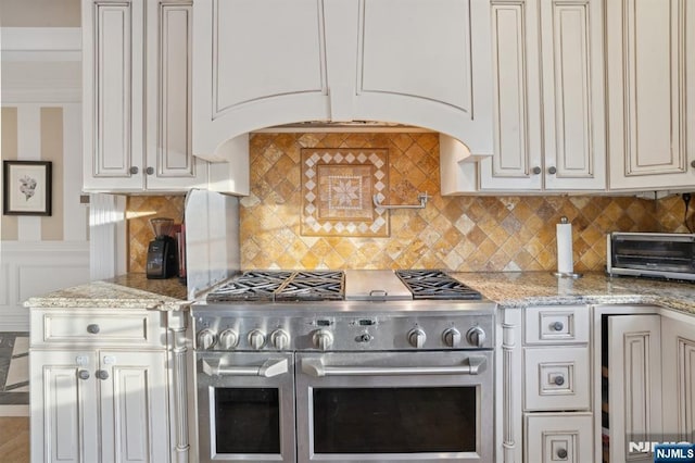 kitchen featuring tasteful backsplash, light stone counters, range with two ovens, and white cabinets