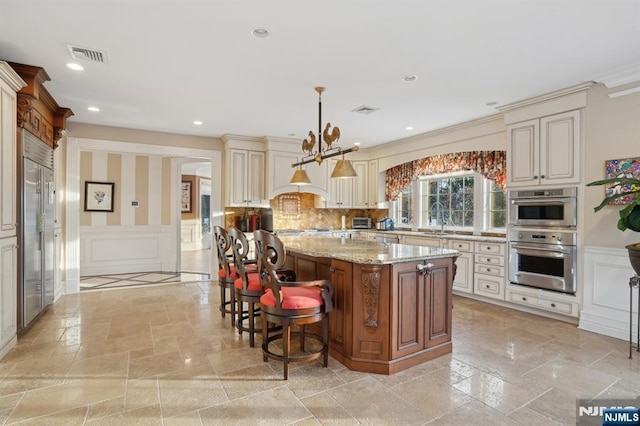 kitchen with cream cabinets, a kitchen island, pendant lighting, and light stone counters