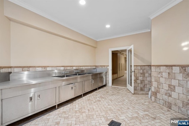 kitchen featuring tile walls, sink, ornamental molding, and stainless steel counters