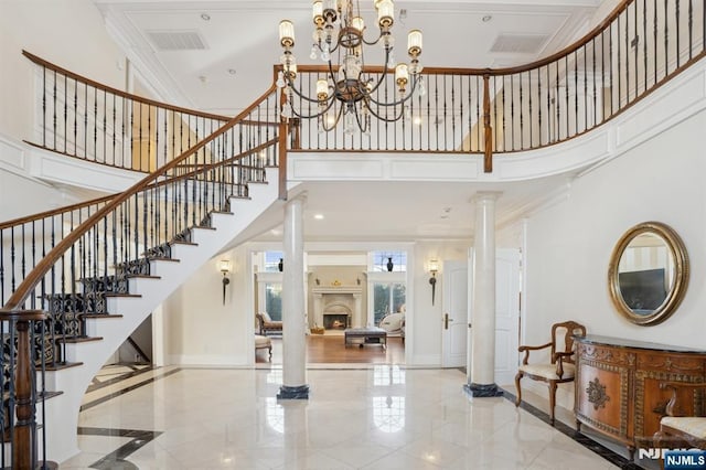 foyer entrance with a towering ceiling, ornamental molding, decorative columns, and a notable chandelier