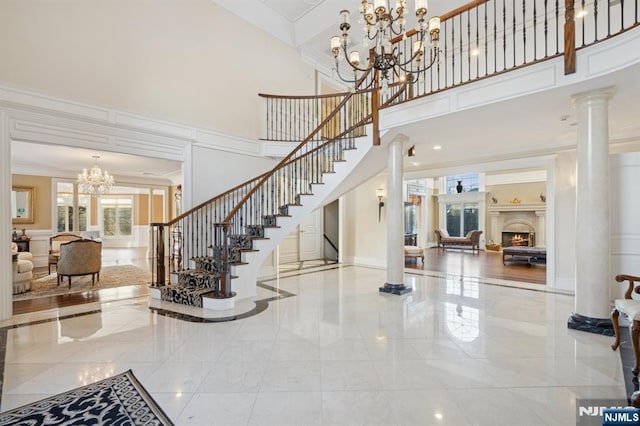 entryway with a towering ceiling, ornamental molding, a chandelier, and decorative columns