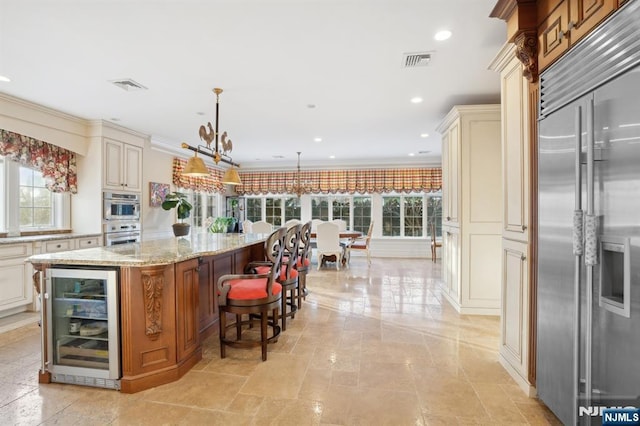 kitchen with appliances with stainless steel finishes, pendant lighting, wine cooler, a center island, and cream cabinetry