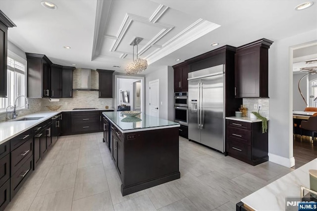 kitchen with wall chimney exhaust hood, sink, hanging light fixtures, appliances with stainless steel finishes, and a kitchen island