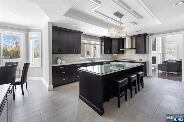 kitchen with pendant lighting, sink, a breakfast bar area, a center island, and wall chimney exhaust hood