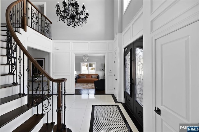 tiled foyer with a towering ceiling, a chandelier, and french doors