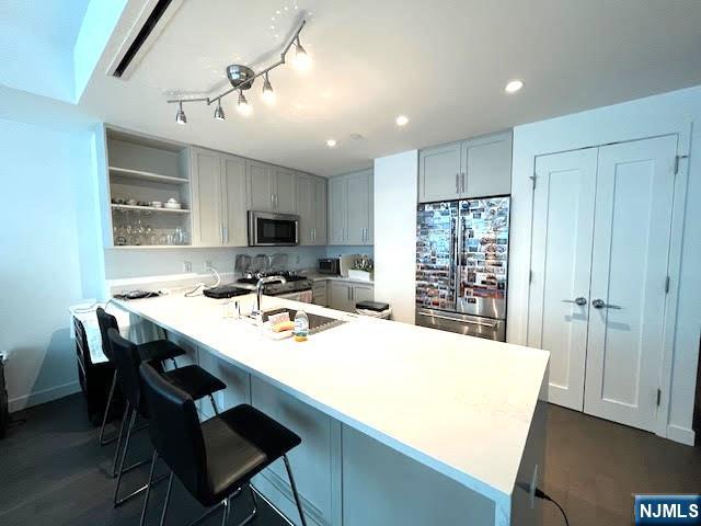 kitchen with gray cabinets, appliances with stainless steel finishes, sink, a kitchen bar, and kitchen peninsula