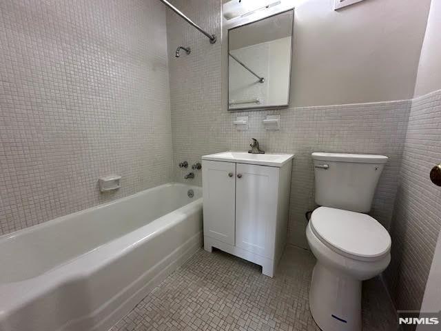 full bathroom featuring tiled shower / bath, tile walls, tile patterned flooring, vanity, and toilet