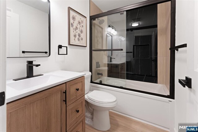 full bathroom with vanity, hardwood / wood-style floors, shower / bath combination with glass door, and toilet