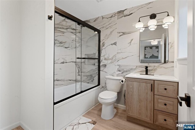 full bathroom featuring toilet, bath / shower combo with glass door, tile walls, vanity, and hardwood / wood-style floors