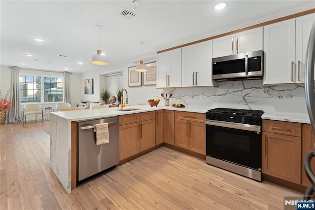 kitchen featuring appliances with stainless steel finishes, pendant lighting, sink, white cabinets, and light hardwood / wood-style floors