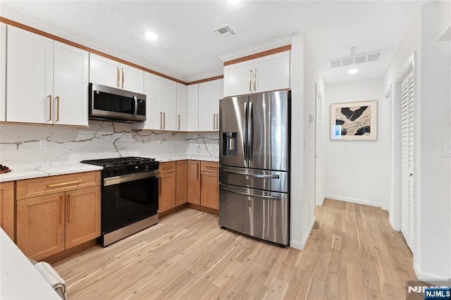 kitchen with appliances with stainless steel finishes, tasteful backsplash, white cabinetry, light hardwood / wood-style floors, and light stone countertops