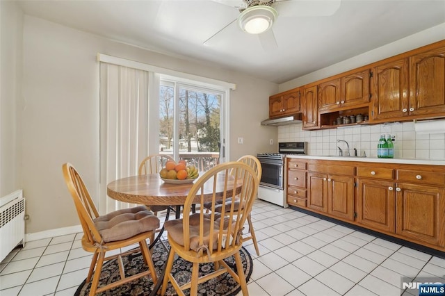 kitchen featuring light tile patterned flooring, radiator heating unit, tasteful backsplash, sink, and stainless steel range with gas stovetop