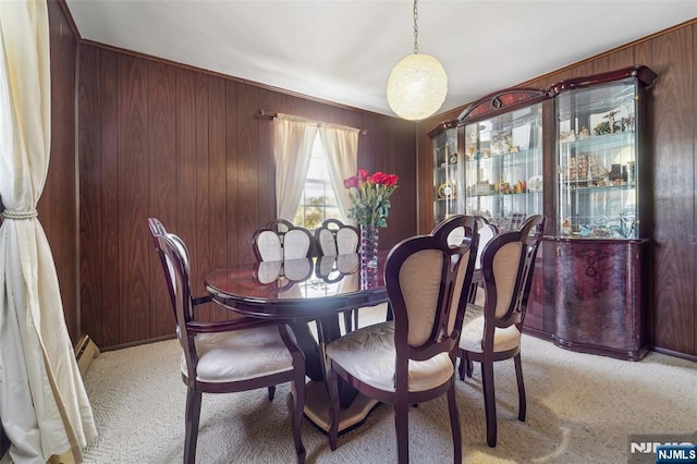 carpeted dining space featuring wood walls