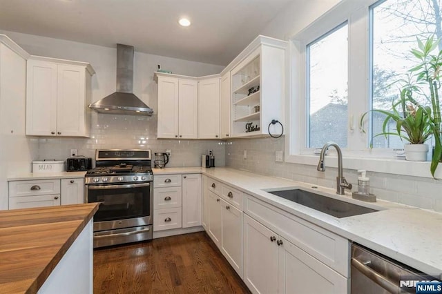 kitchen featuring wood counters, wall chimney exhaust hood, sink, appliances with stainless steel finishes, and white cabinets