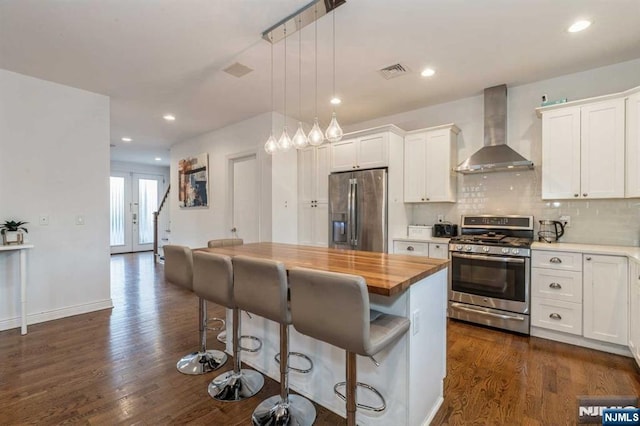 kitchen featuring a kitchen bar, white cabinetry, decorative light fixtures, stainless steel appliances, and wall chimney range hood