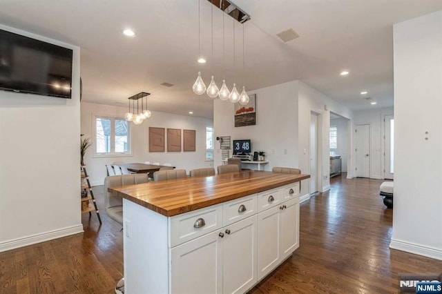 kitchen featuring dark wood-type flooring, butcher block countertops, white cabinetry, decorative light fixtures, and a center island