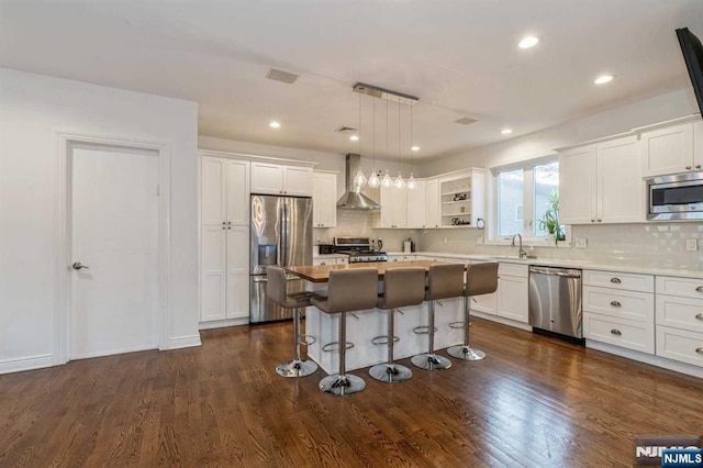 kitchen with appliances with stainless steel finishes, a center island, wall chimney range hood, and decorative light fixtures