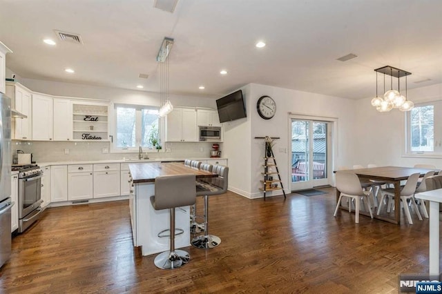 kitchen with decorative light fixtures, a center island, appliances with stainless steel finishes, dark hardwood / wood-style floors, and white cabinets