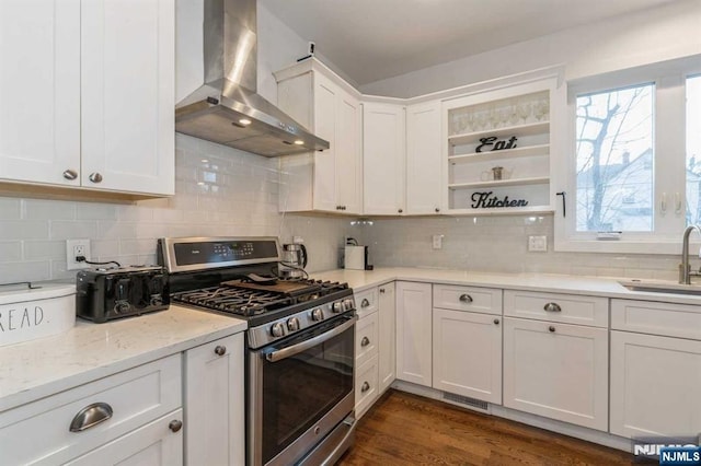 kitchen featuring sink, backsplash, stainless steel gas range oven, white cabinets, and wall chimney exhaust hood