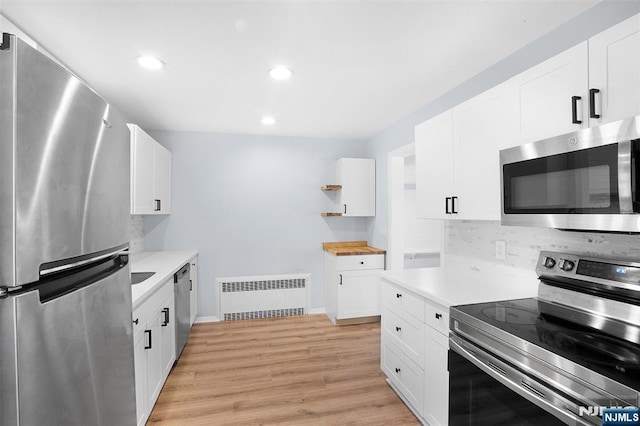 kitchen featuring light hardwood / wood-style flooring, white cabinetry, backsplash, radiator heating unit, and stainless steel appliances