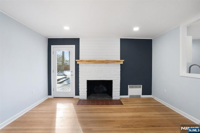 unfurnished living room with ornamental molding, radiator heating unit, a fireplace, and light hardwood / wood-style flooring