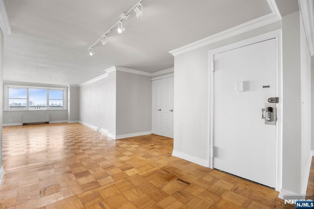 interior space with radiator heating unit, track lighting, ornamental molding, and light parquet floors