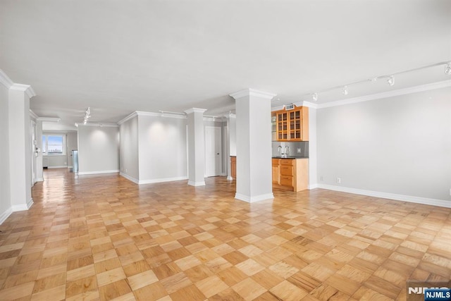 unfurnished living room with crown molding, light parquet flooring, bar area, and decorative columns