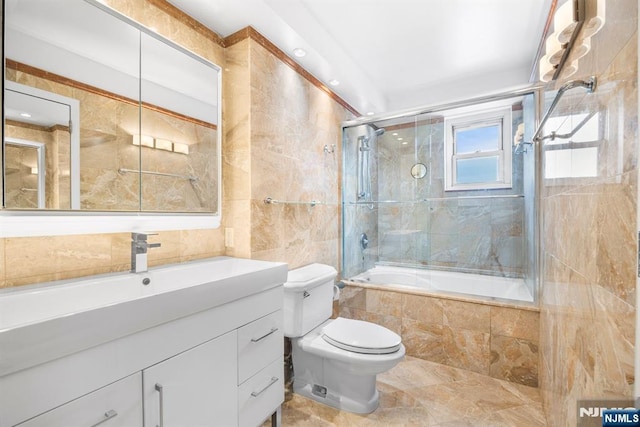 full bathroom with tile walls, vanity, enclosed tub / shower combo, and toilet