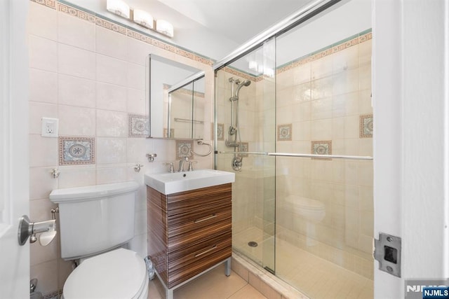 bathroom with toilet, a shower with shower door, tile patterned flooring, and tile walls