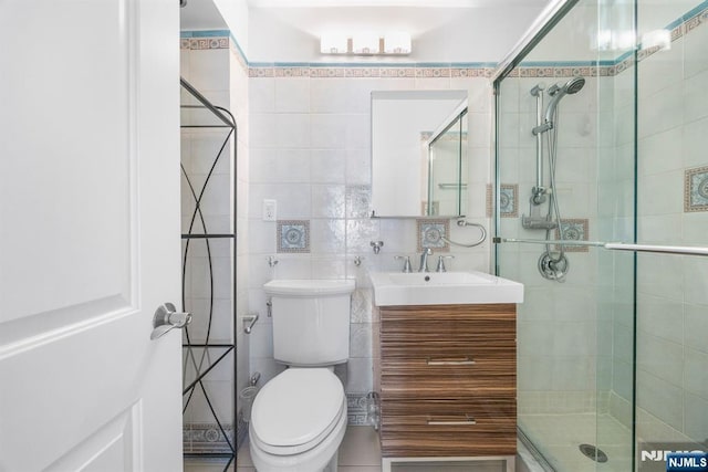 bathroom featuring toilet, tile walls, vanity, and a shower with shower door